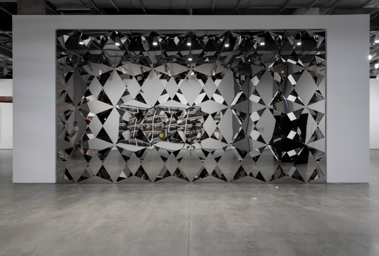 A sculpture of stainless steel panels with mirrored elements creating a geometric pattern on the wall.