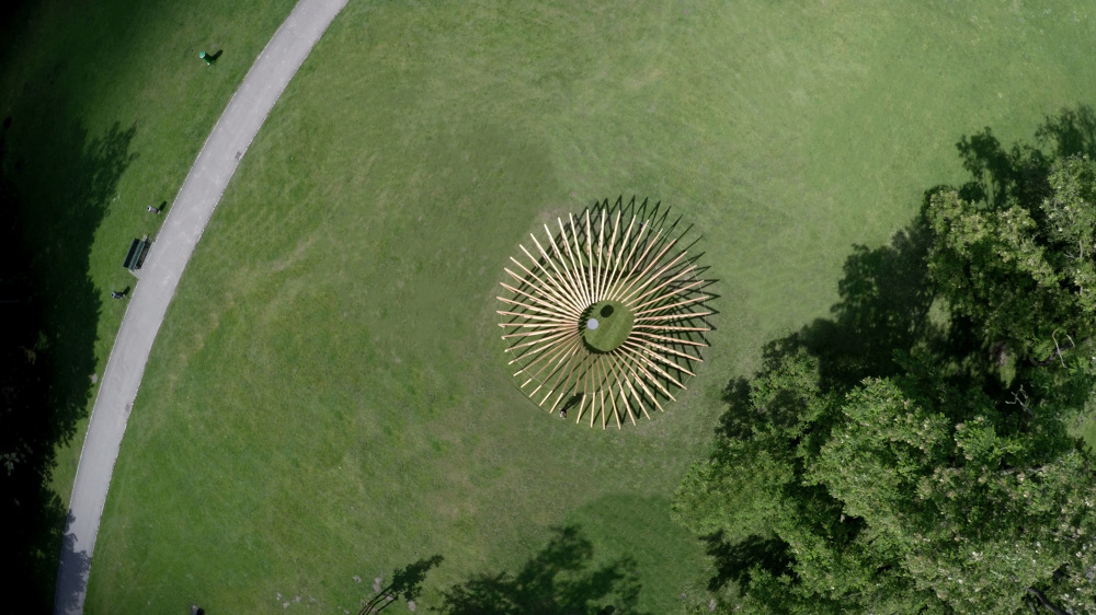 A wooden triangular structure with LED branches forming a circle in an open field.
