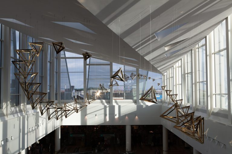 The room features a suspended sculpture with geometric shapes made from coated stainless steel.