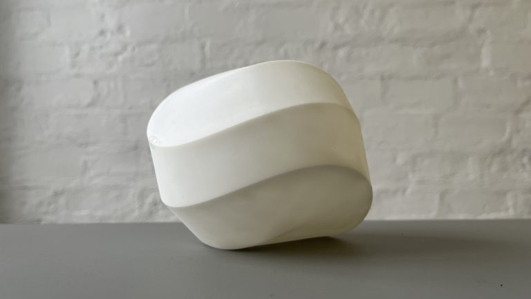 Modern art sculpture of resin with wavy edges on a white surface.