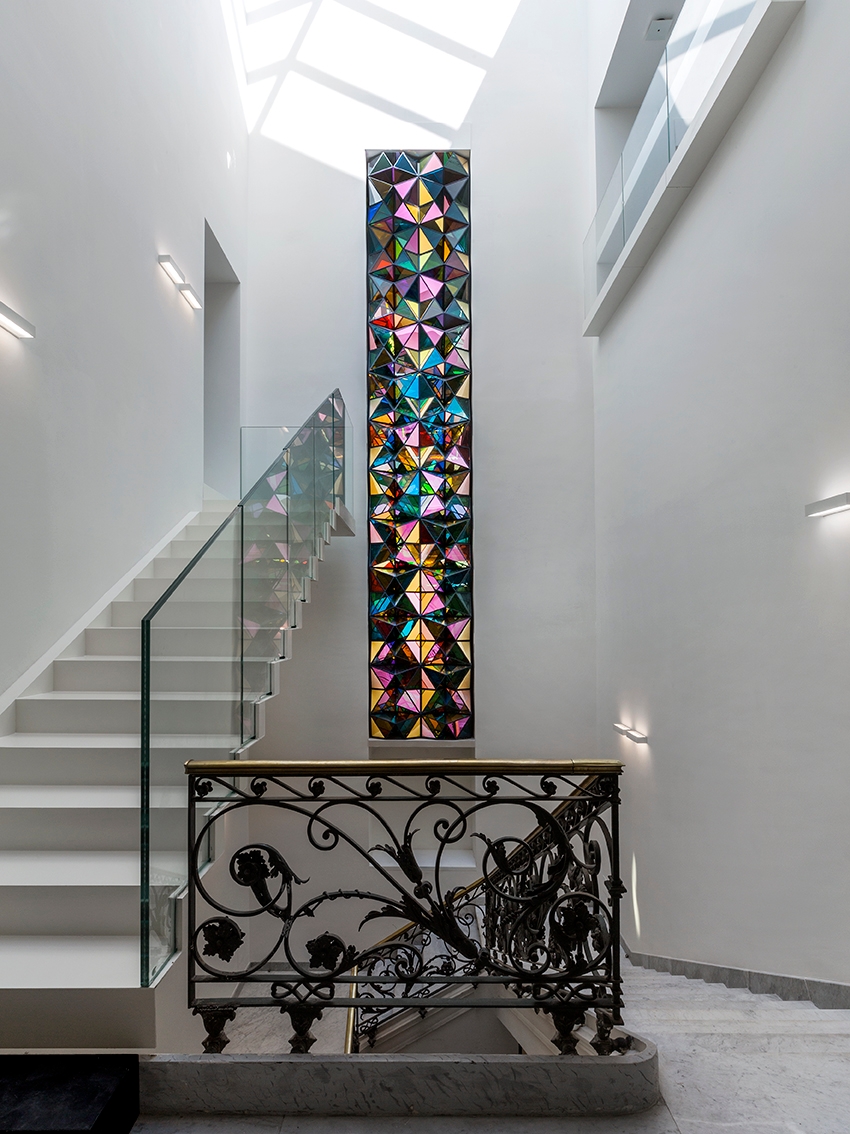 Colorful stained glass artwork hanging on wall with black wrought iron railing.