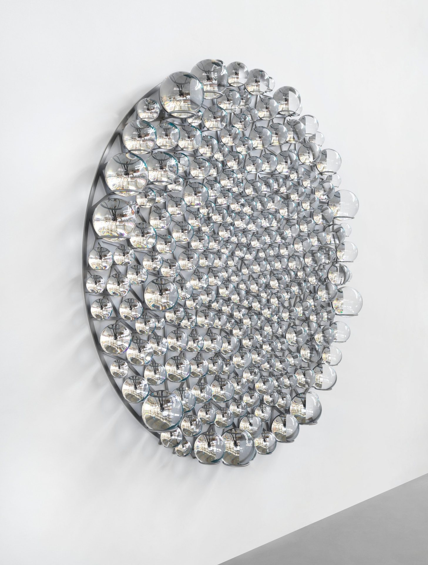 Glass and steel sculpture with circular pattern, installed on wall.