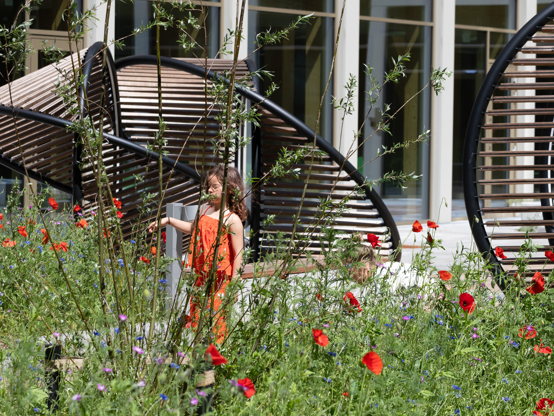 The young girl stands on the grass under a metal structure that has red flowers and integrated lighting.