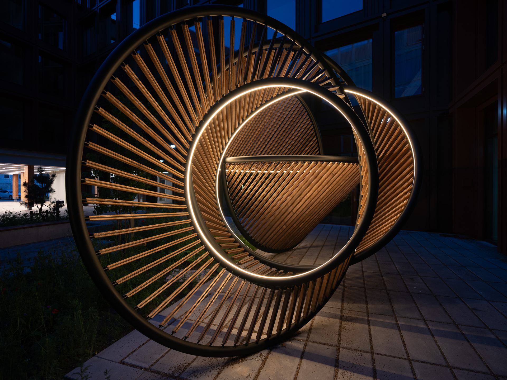Circular sculpture of metal and wood with illuminated rings.