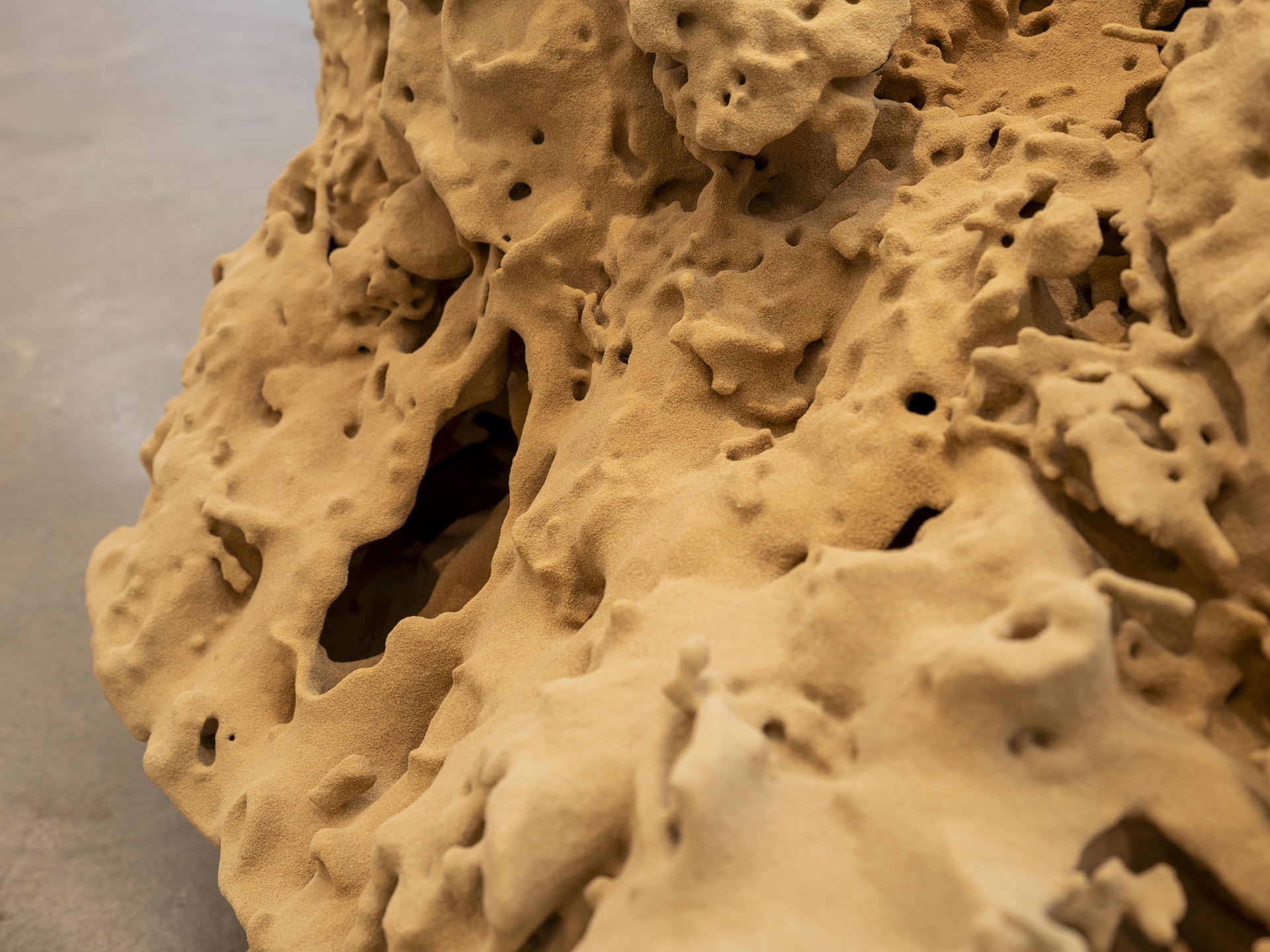 The sculpture is made of sand and displayed on a white pedestal.
