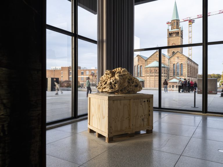 Square sand sculpture on wooden pallet inside gallery.