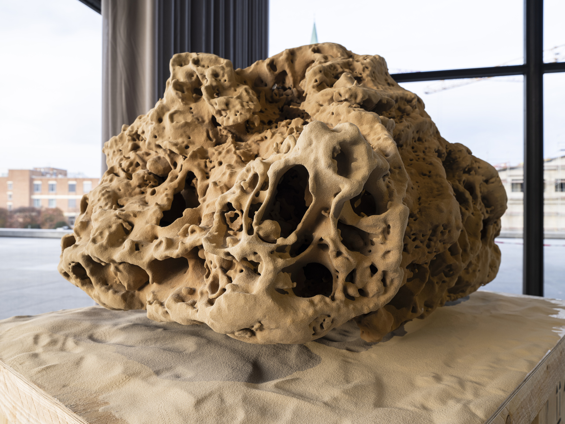 A natural rock sculpture with various porous textures, resembling a sandy coastline grain.