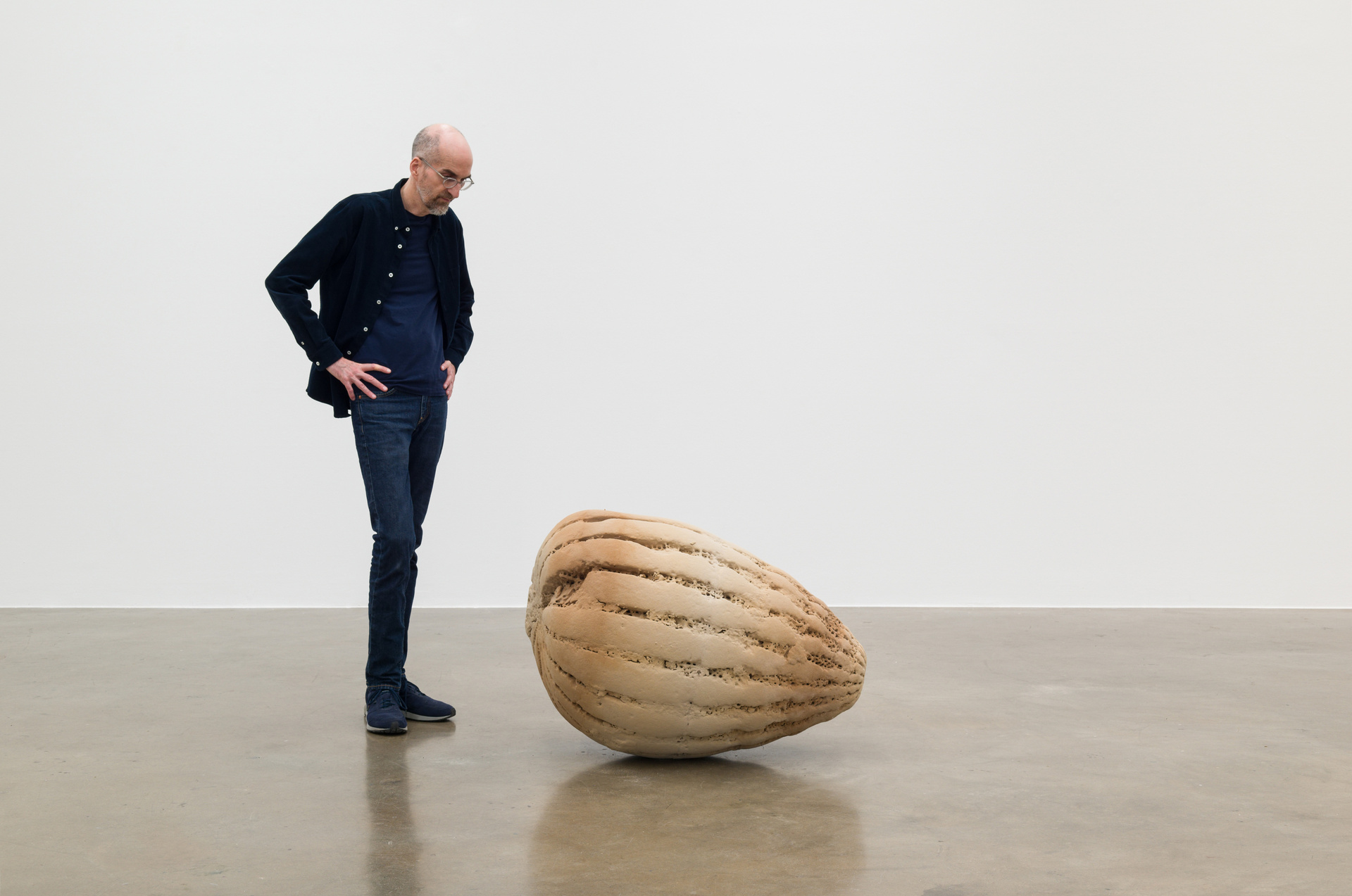The man stands next to a large sculpture of sand and wood.
