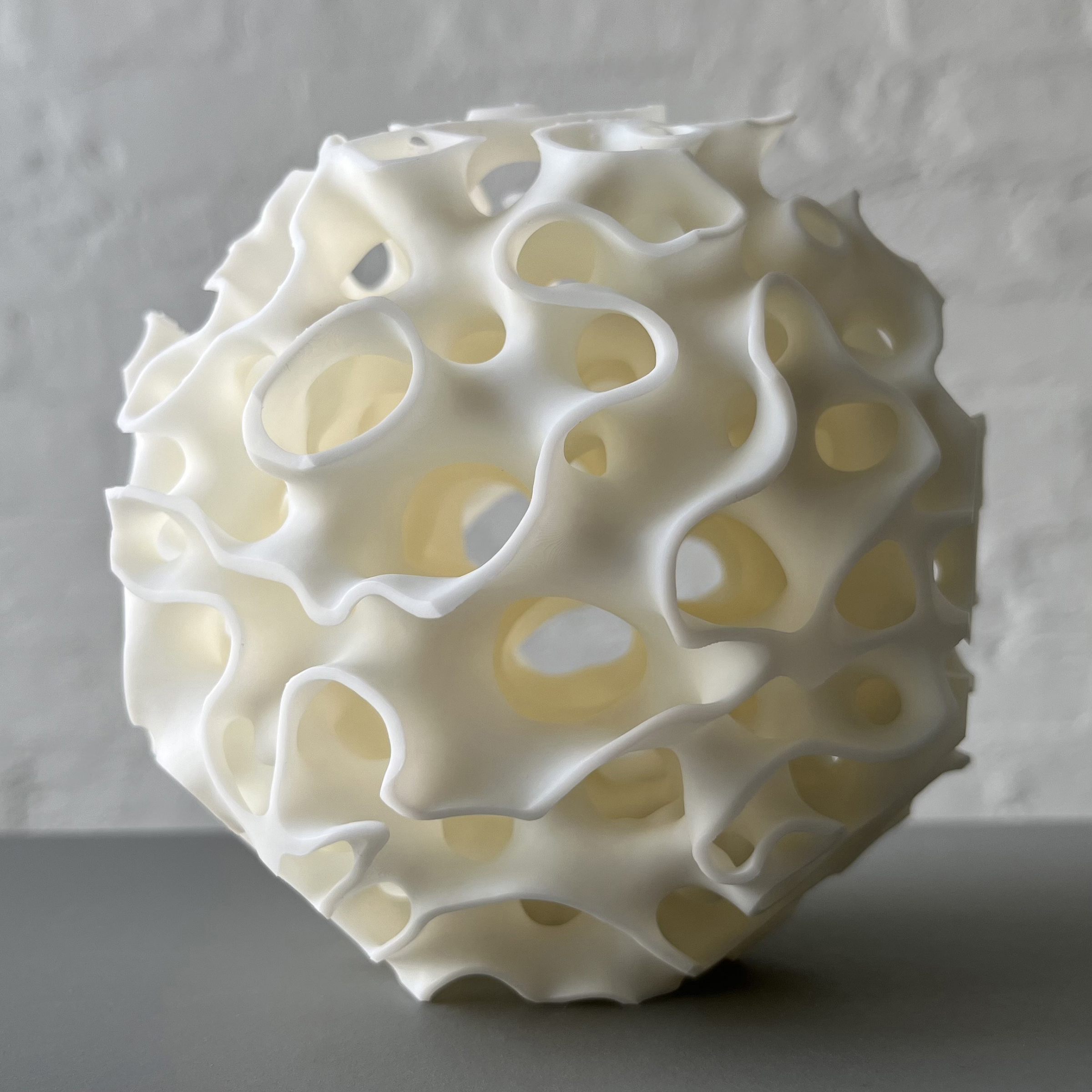 Resin sculpture of a porous polyhedron with wavy edges, displayed in an indoor space.
