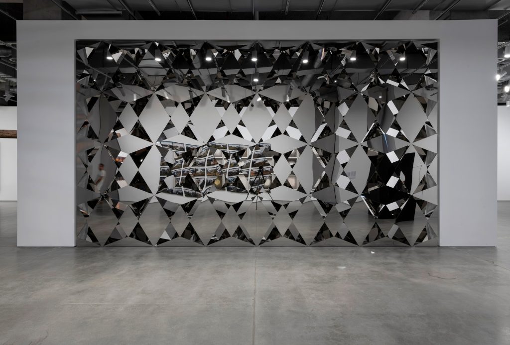 Less Ego Wall is a mirror-clad wall made of stainless steel and diamond-shaped mirror panels.