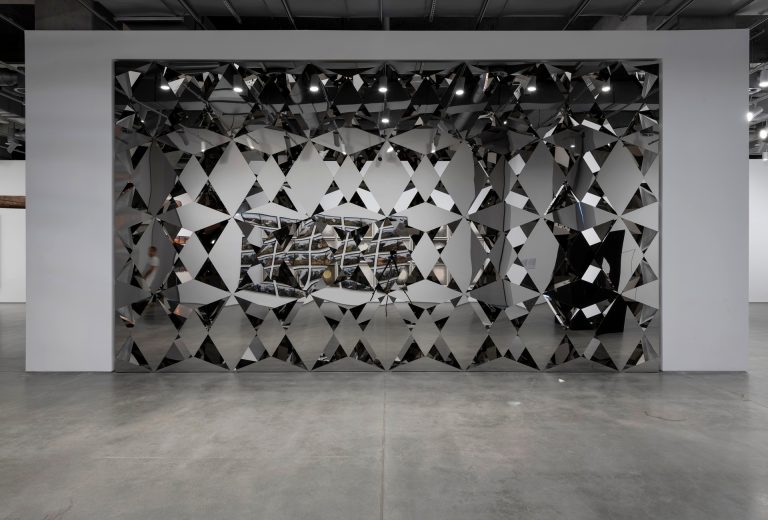 Less Ego Wall is a mirror-clad wall made of stainless steel and diamond-shaped mirror panels.