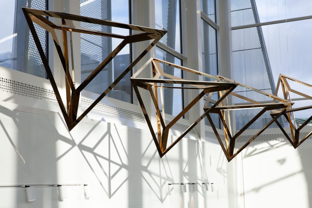 Crystal Loop, a sculpture of coated stainless steel, hangs in a modern building.