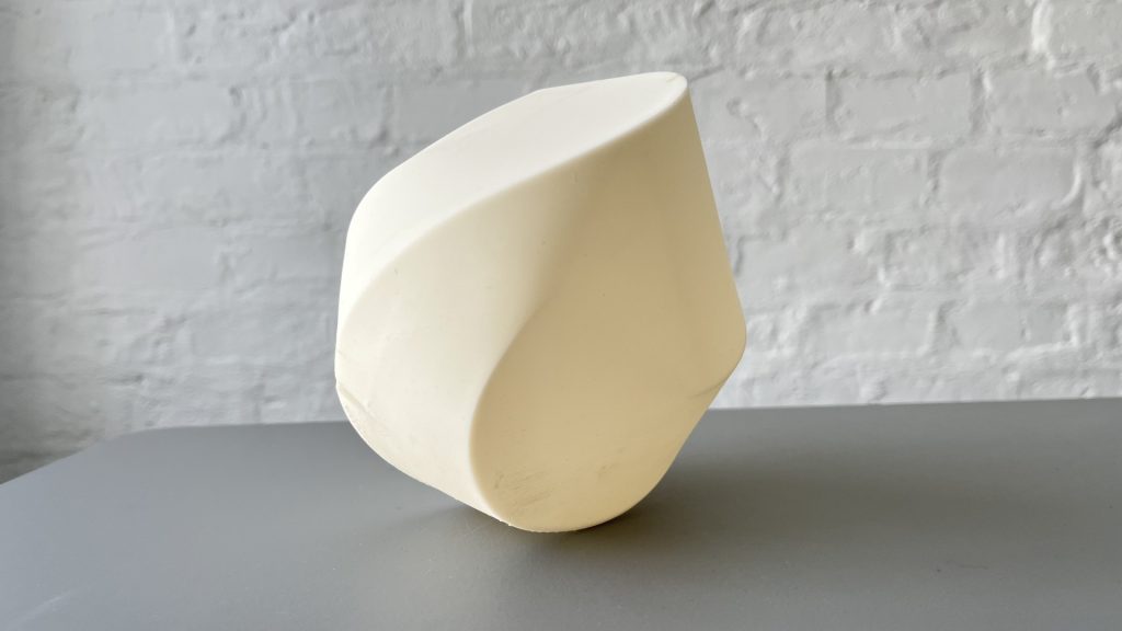White 3D-printed resin sculpture sits on gray surface against white brick wall.