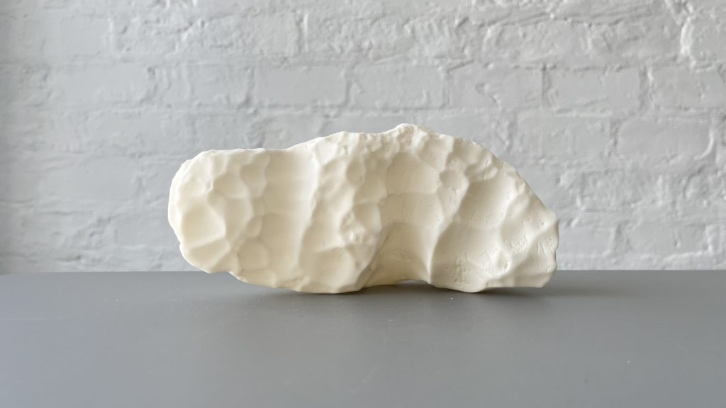 White 3D-printed resin sculpture sits on table against white brick wall.