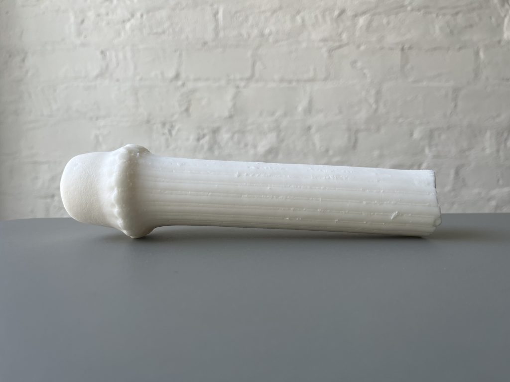 3D printed resin object sits on gray surface against white brick wall.