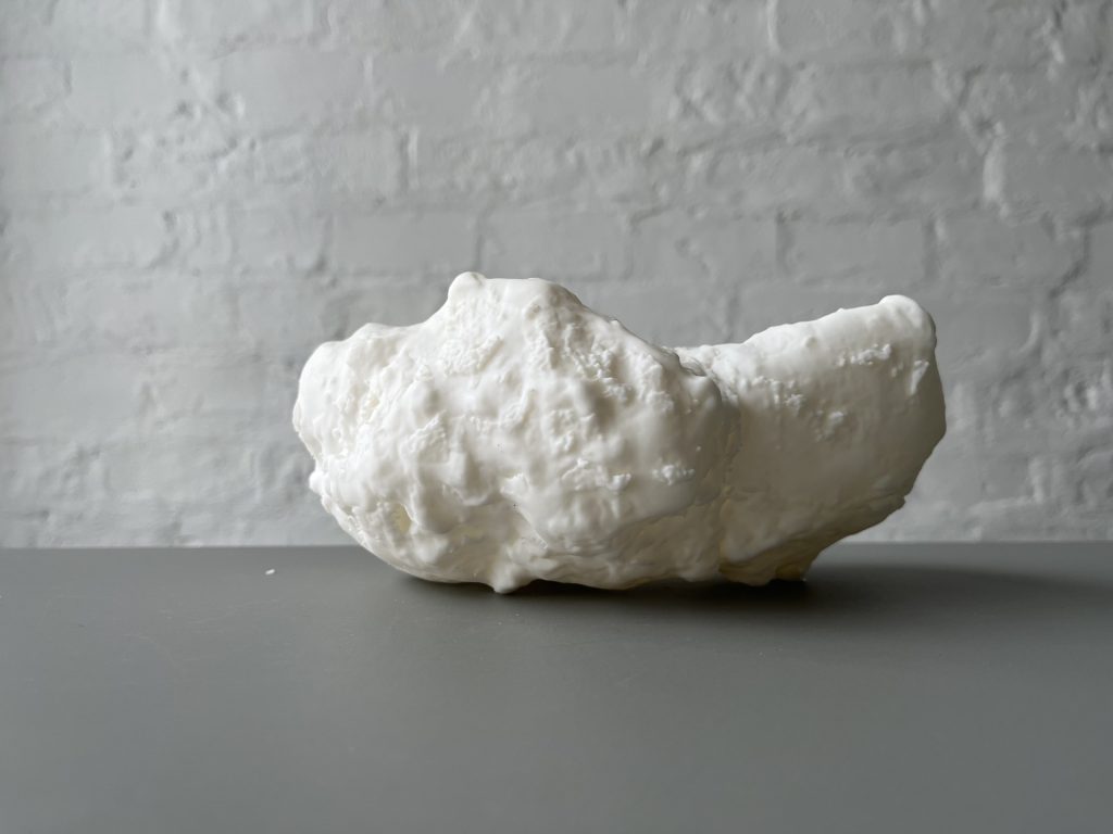 White 3D printed resin object sits on gray surface against white brick wall.