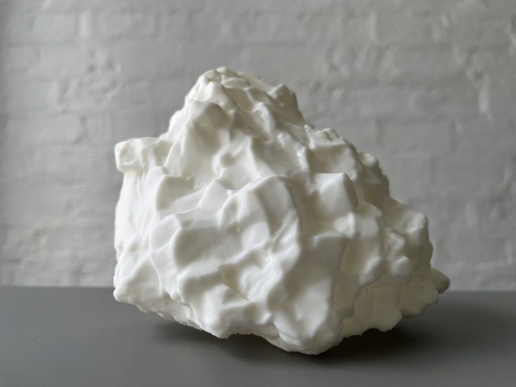 White 3D printed resin sculpture sits on gray surface against white wall.