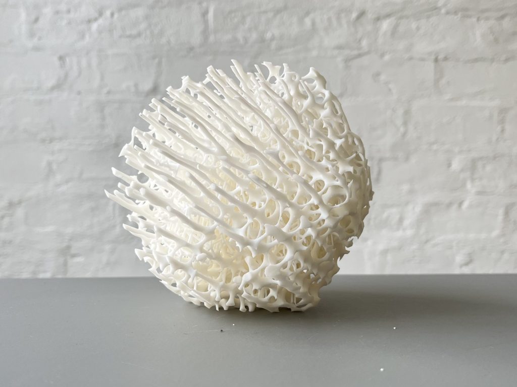 3D printed resin sculpture sits on a white surface against a white brick wall.