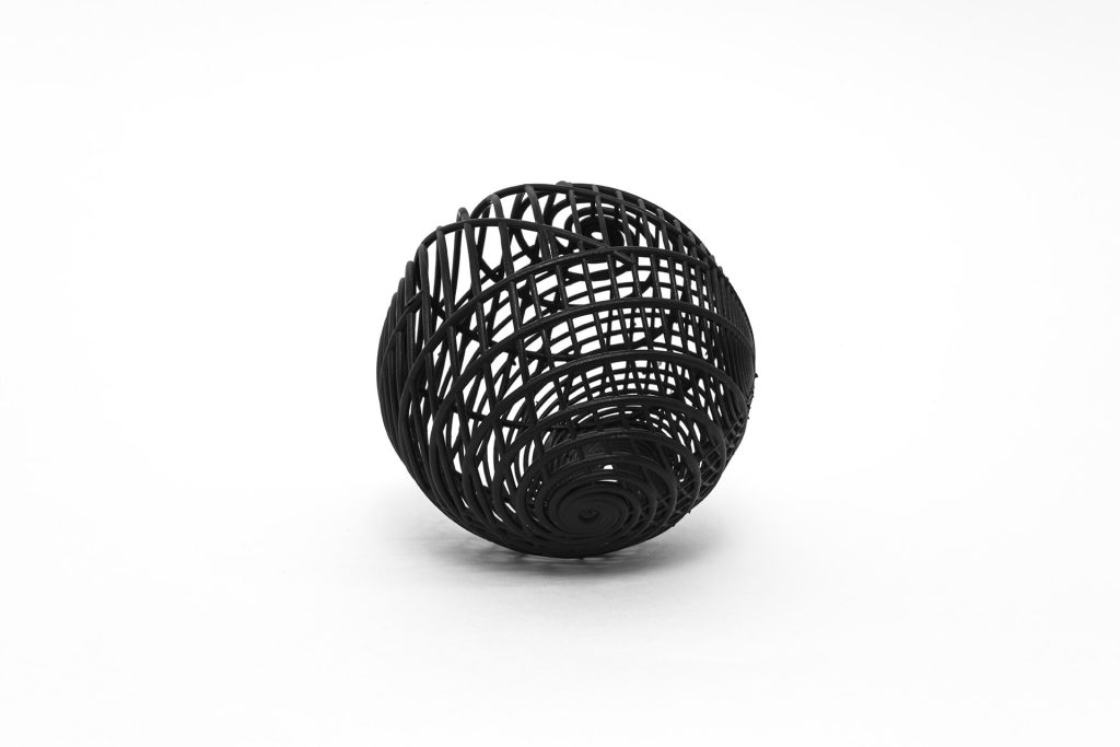 A black, 3D-printed resin sphere with spiral patterns sits on a white surface.