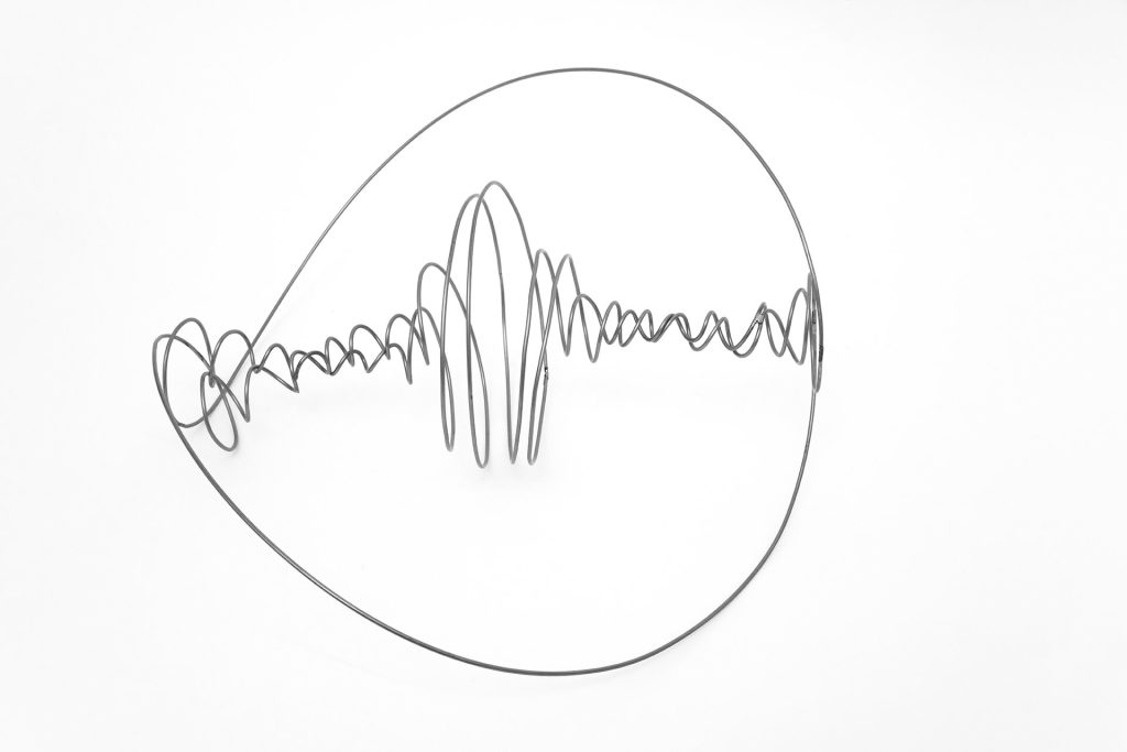 A wire sculpture forms a circular frame with a wavy, oscillating line inside on a white background.