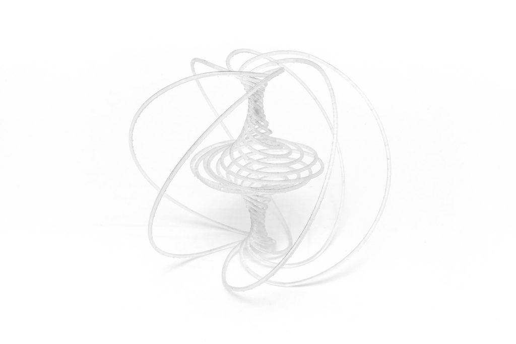 A white, 3D-printed resin sculpture with interwoven loops and spirals sits on a plain surface.
