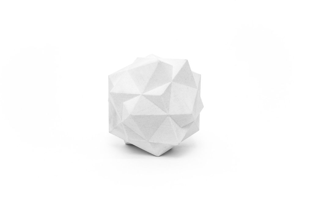 A white, 3D-printed resin polyhedron with geometric facets sits on a plain surface.