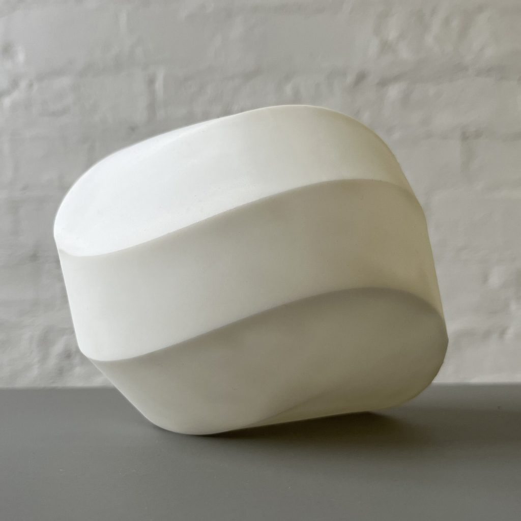A white 3D printed resin module from the Kaleidocycloids project sits on a gray surface against a white brick wall.