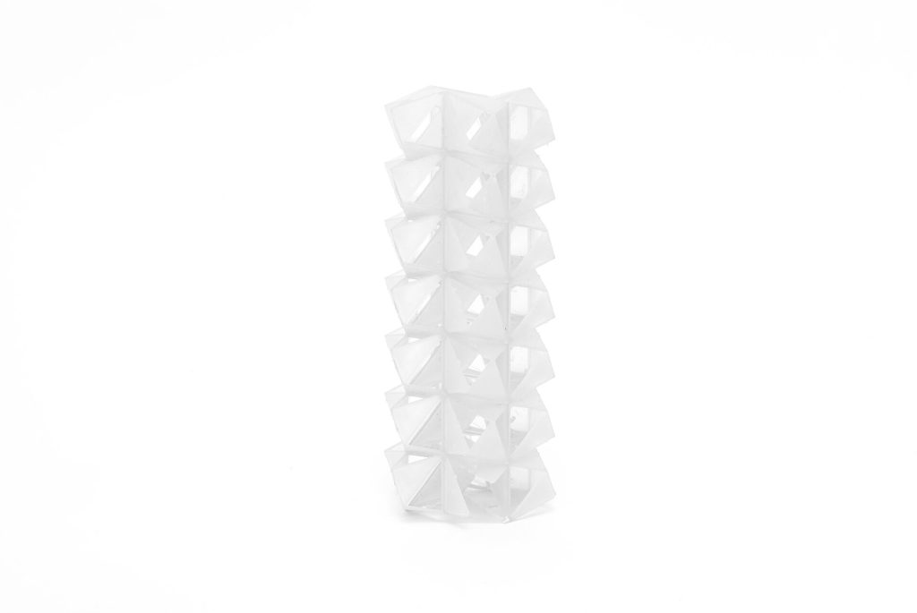 A white, 3D-printed resin tower composed of stacked geometric modules stands vertically on a plain background.