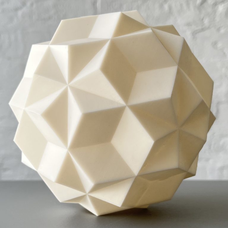 A 3D printed resin Phi Stars model sits on a gray surface against a white wall.