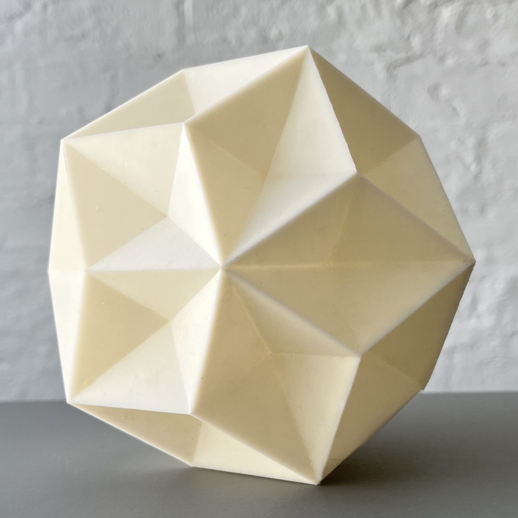 A 3D printed resin Phi Stars model sits on a gray surface against a white wall.