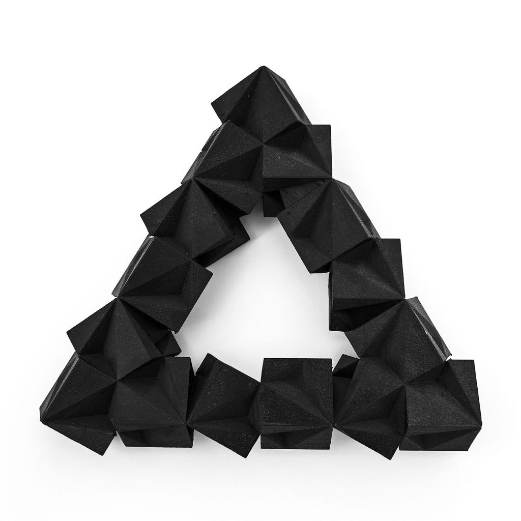 A black 3D printed resin triangle of interlocking cubes sits on a white surface.