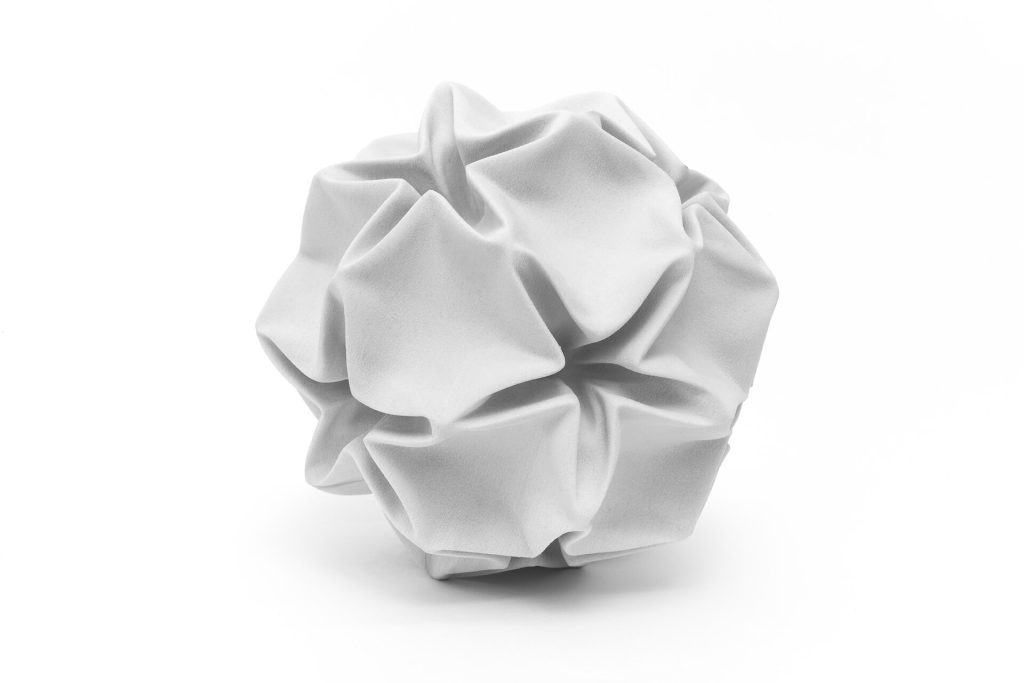 A white, crumpled sphere made of 3D-printed resin sits on a plain surface.