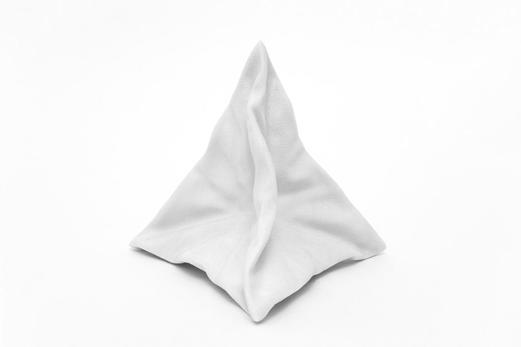 A white, 3D-printed resin object resembling a deformed pyramid sits on a plain surface.
