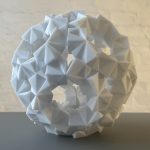 A white 3D-printed resin torus with triangular facets sits on a gray surface.