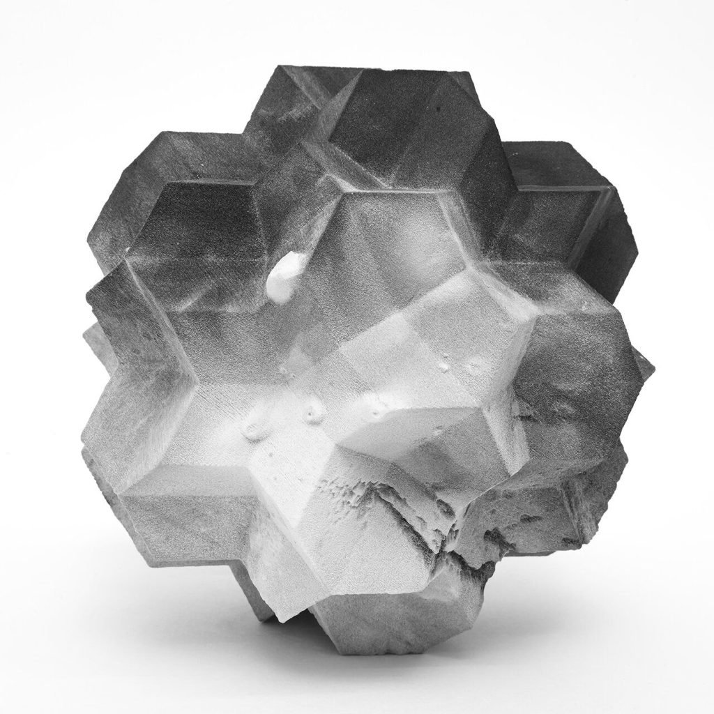 A 3D printed resin object displays a faceted polyhedral form with textured surfaces.