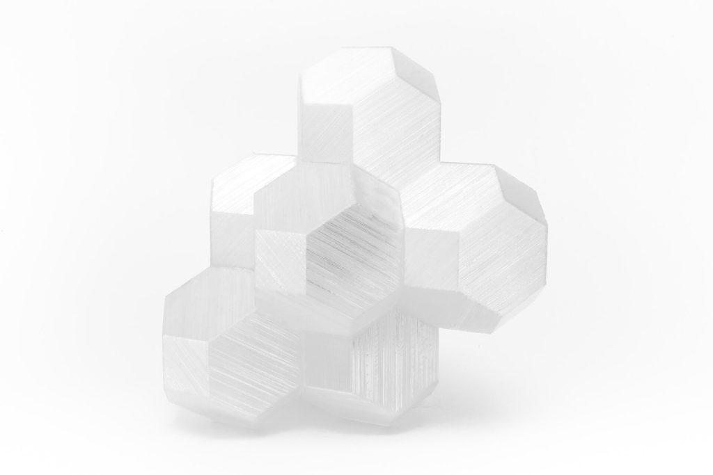 A white, 3D-printed resin model of interlocking truncated octahedra demonstrates a space-filling tessellation on a plain background.