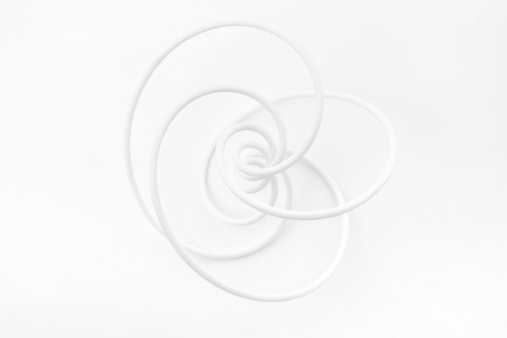 A white 3D-printed resin spiral knot model rests on a plain surface.