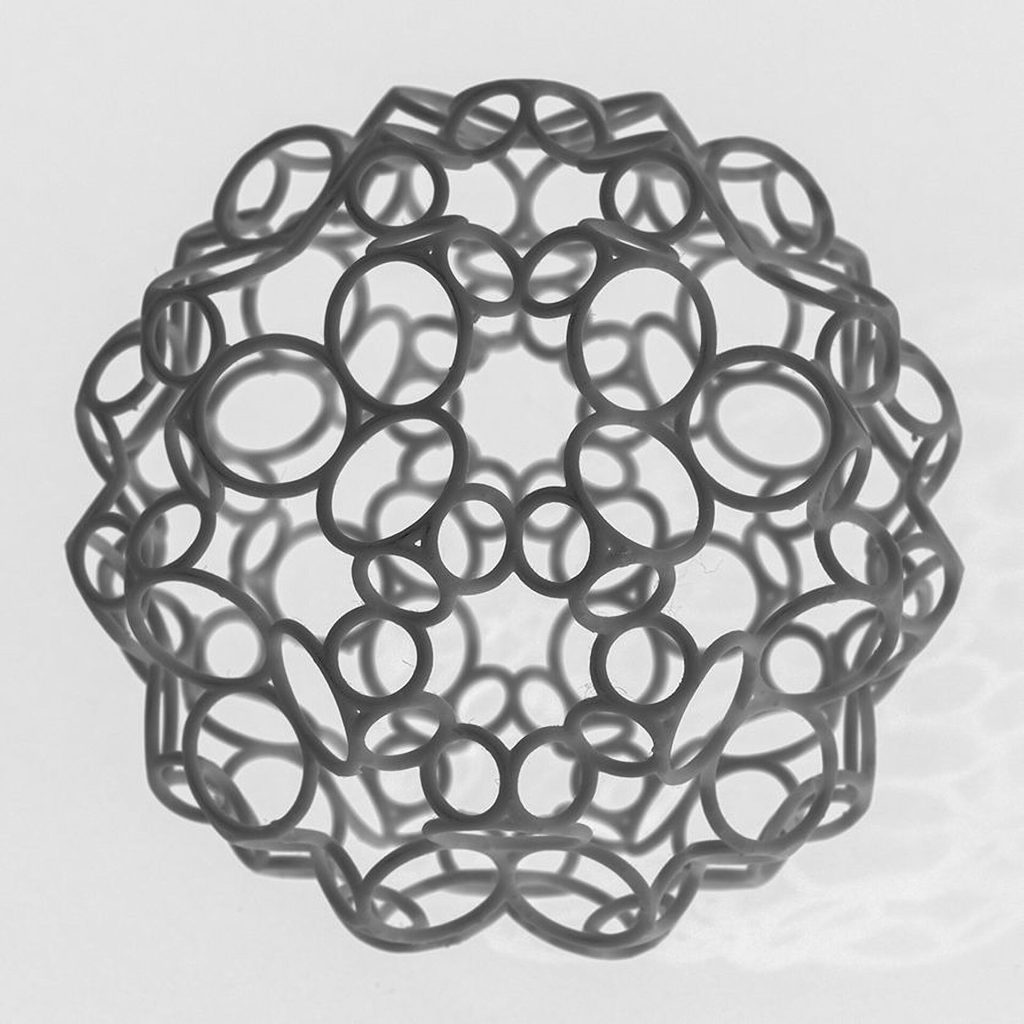 A 3D printed resin sphere has a lattice of interlocking rings on a white background.