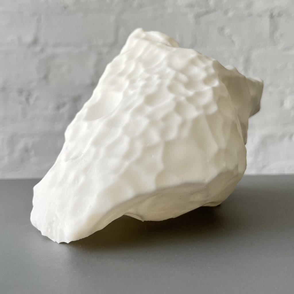 A white 3D printed resin block with a bumpy surface sits on a gray table against a white brick wall.