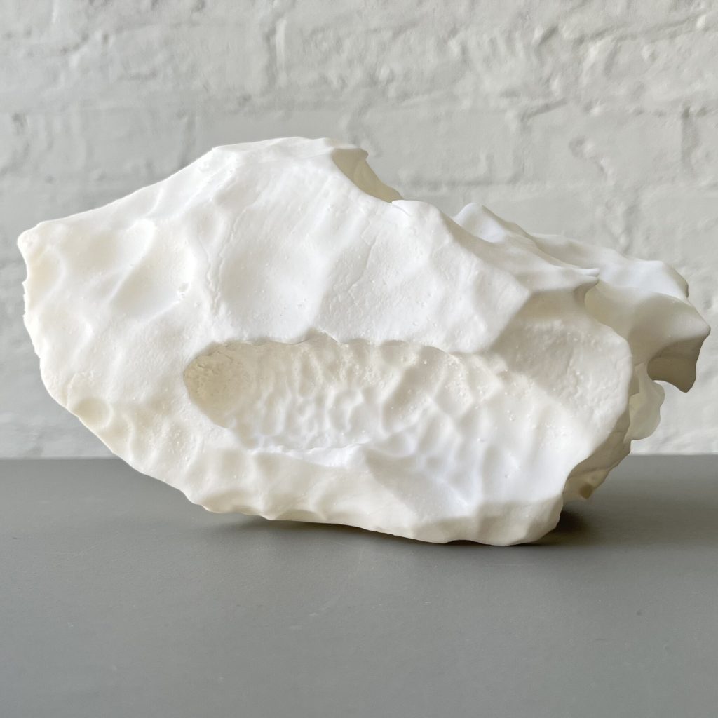 A white 3D printed resin sculpture sits on a gray surface against a white brick wall.