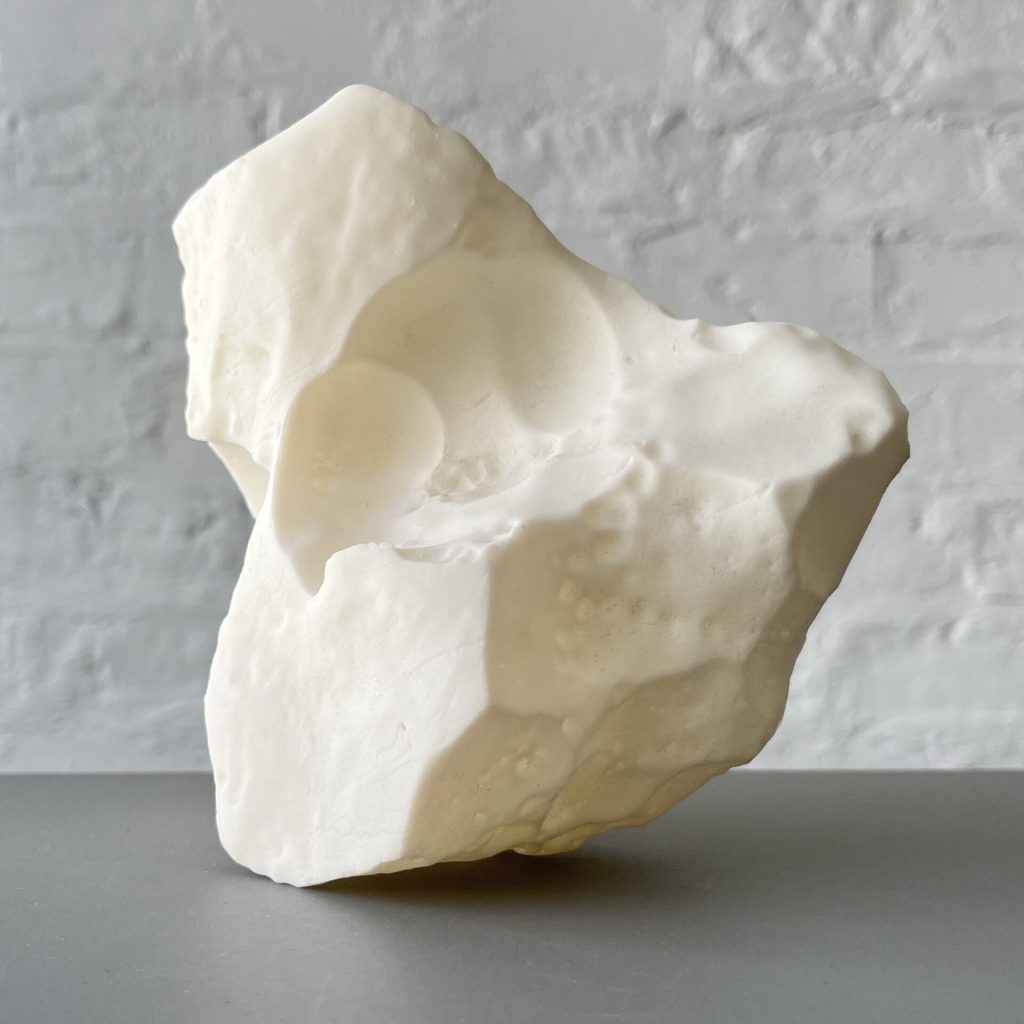 A white 3D printed resin block with smooth indentations sits on a gray surface against a white brick wall.