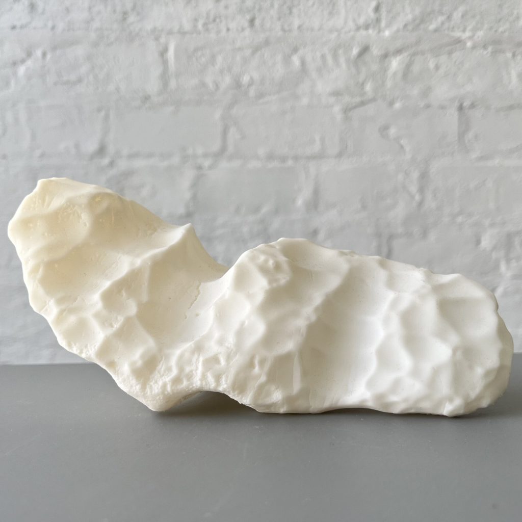 A white 3D printed resin object sits on a gray surface against a white brick wall.