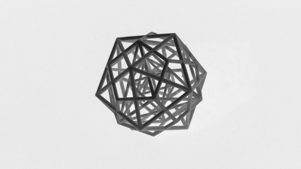 A black 3D-printed resin geometric structure composed of interlocking lines forms a complex polyhedral shape on a white surface.