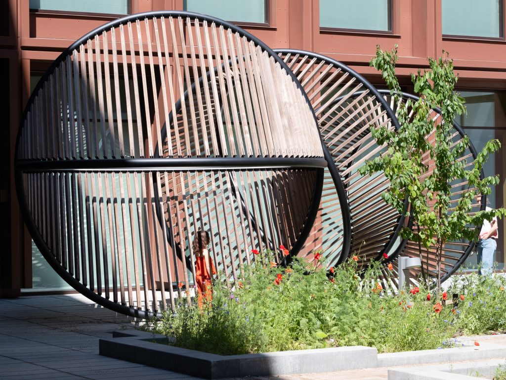 Painted stainless steel rings with wooden slats sit in a garden bed with flowers.