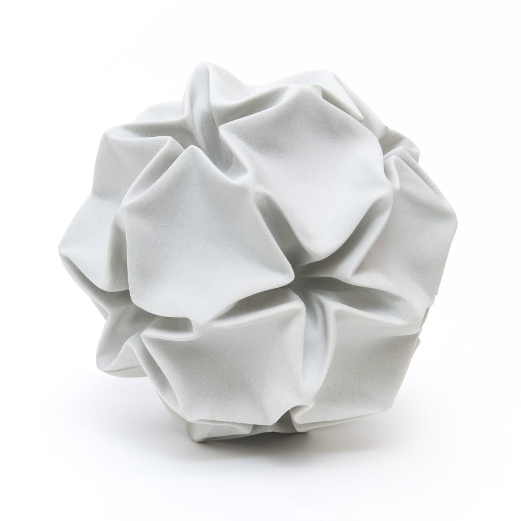 A white 3D-printed plaster model of a deformed rhombic triacontahedron sits on a surface.