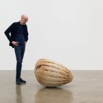 A man stands beside a large 3D printed sand sculpture of an enlarged grain.