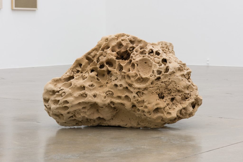 A beige 3D printed sand sculpture sits on a concrete floor in a gallery.