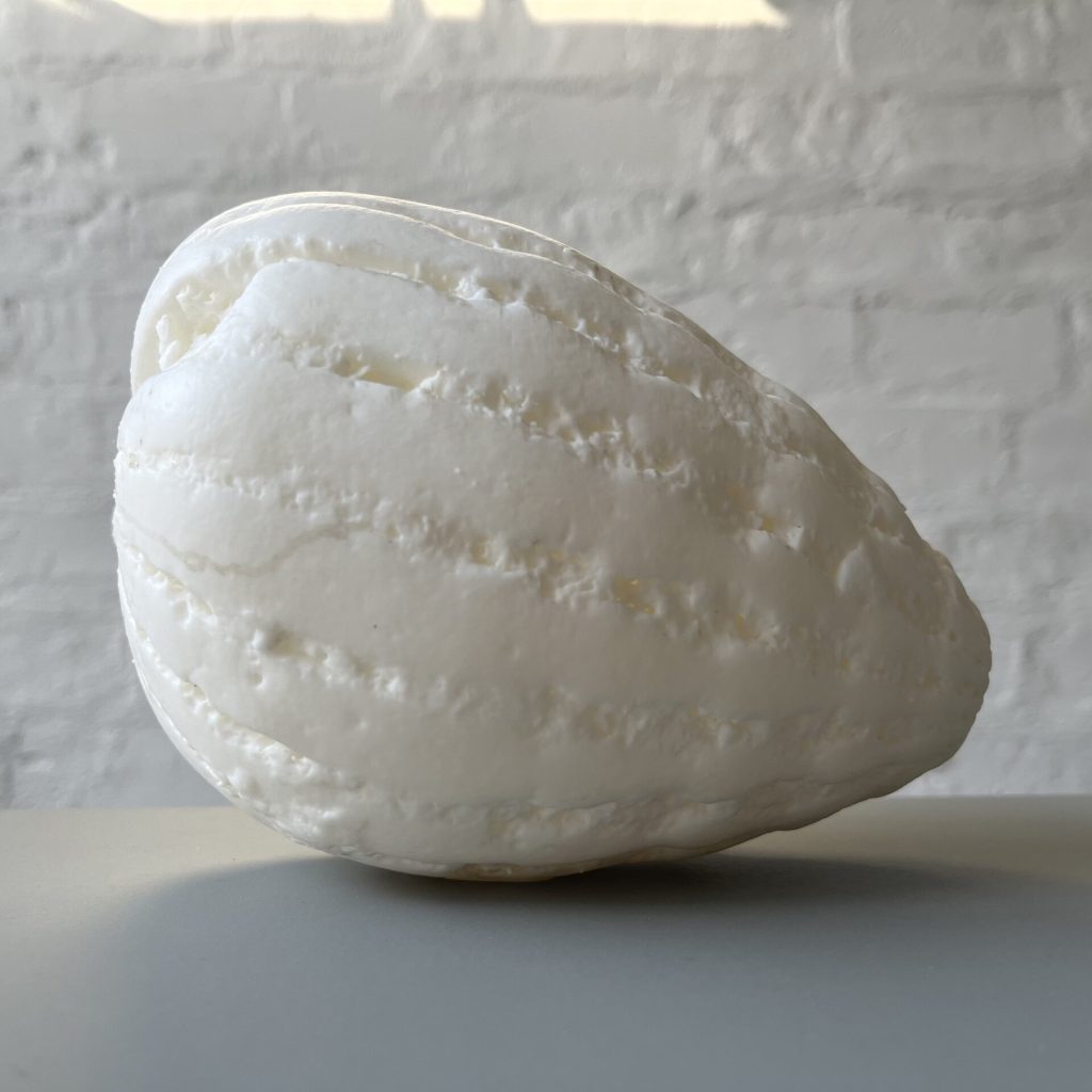 A white 3D printed resin object sits on a gray surface against a white brick wall.
