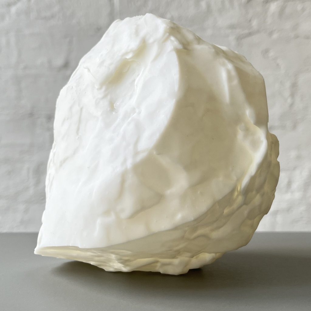 A white 3D printed resin object with a textured surface sits on a gray surface against a white brick wall.