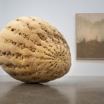 A 3D-printed sand sculpture sits on the floor next to a sand painting on the wall.